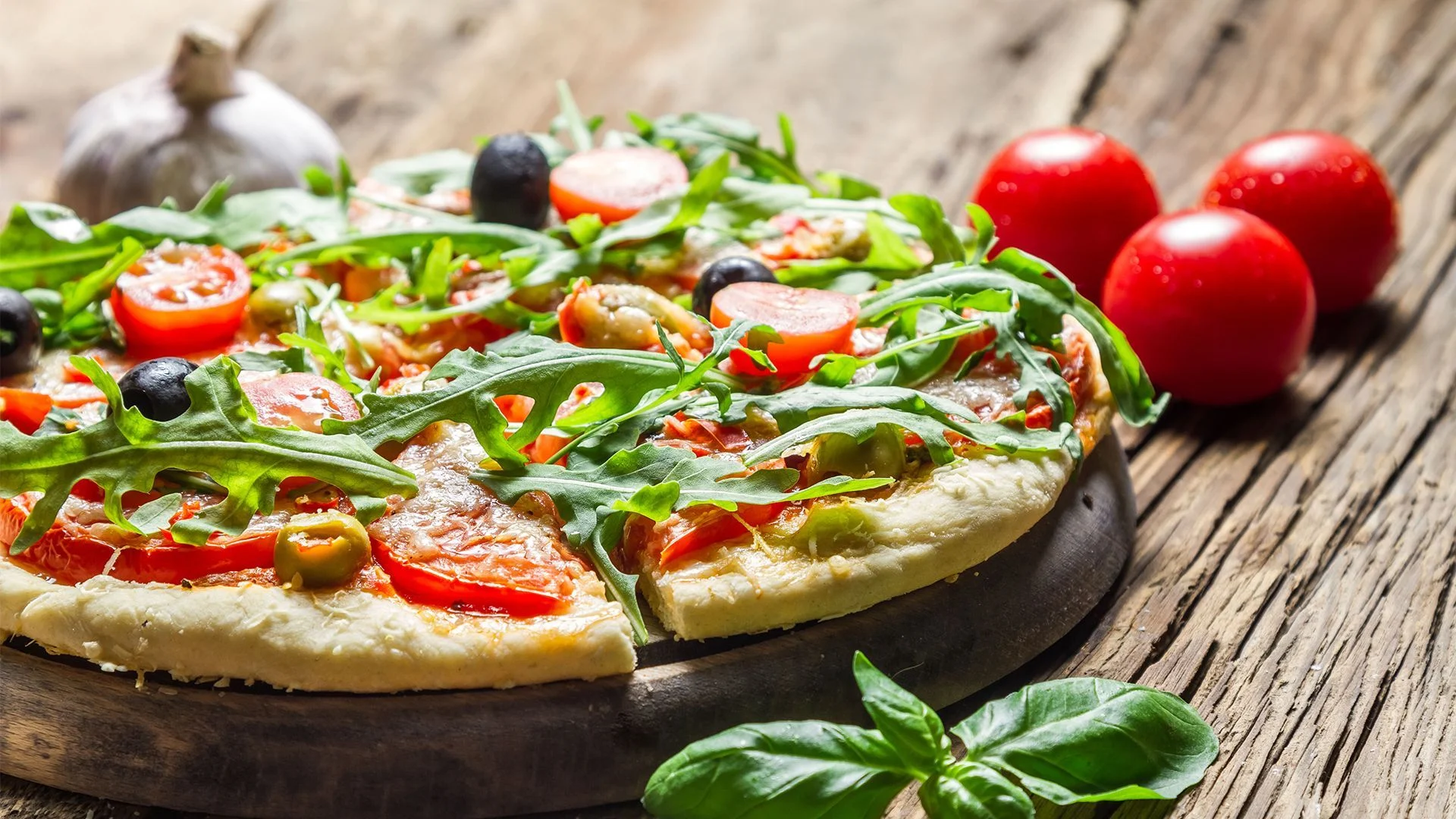 Freshly topped pizza with tomatoes, greens, and olives